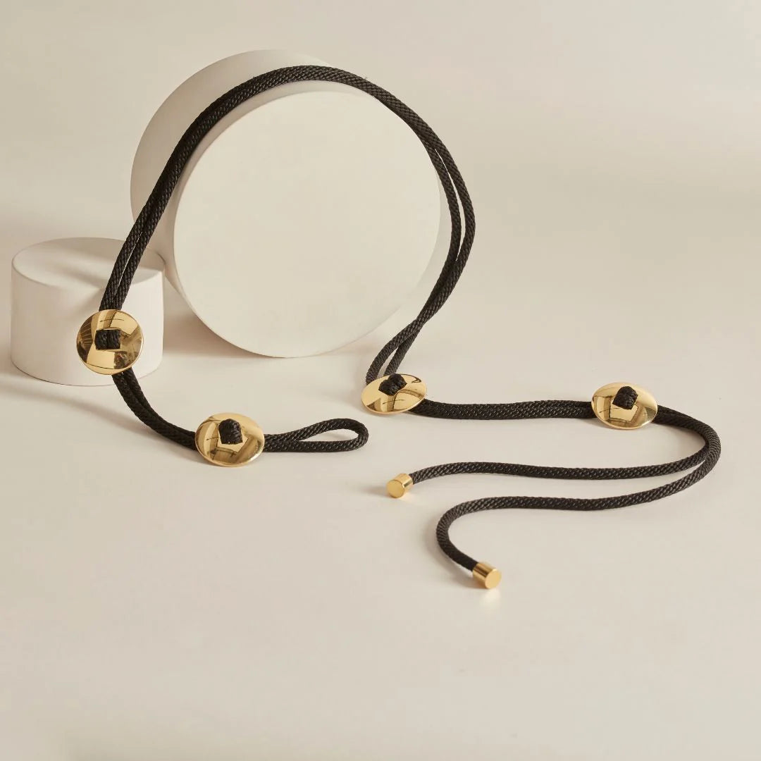 Black cord belt with gold accents on a neutral background