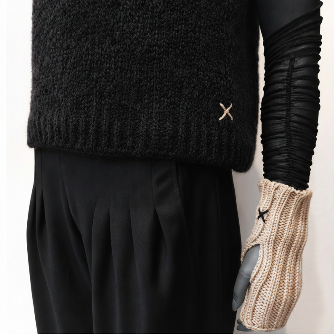 A close-up of a mannequin wearing a black knit sweater, black pleated trousers, and a beige knit glove with a small black star detail.