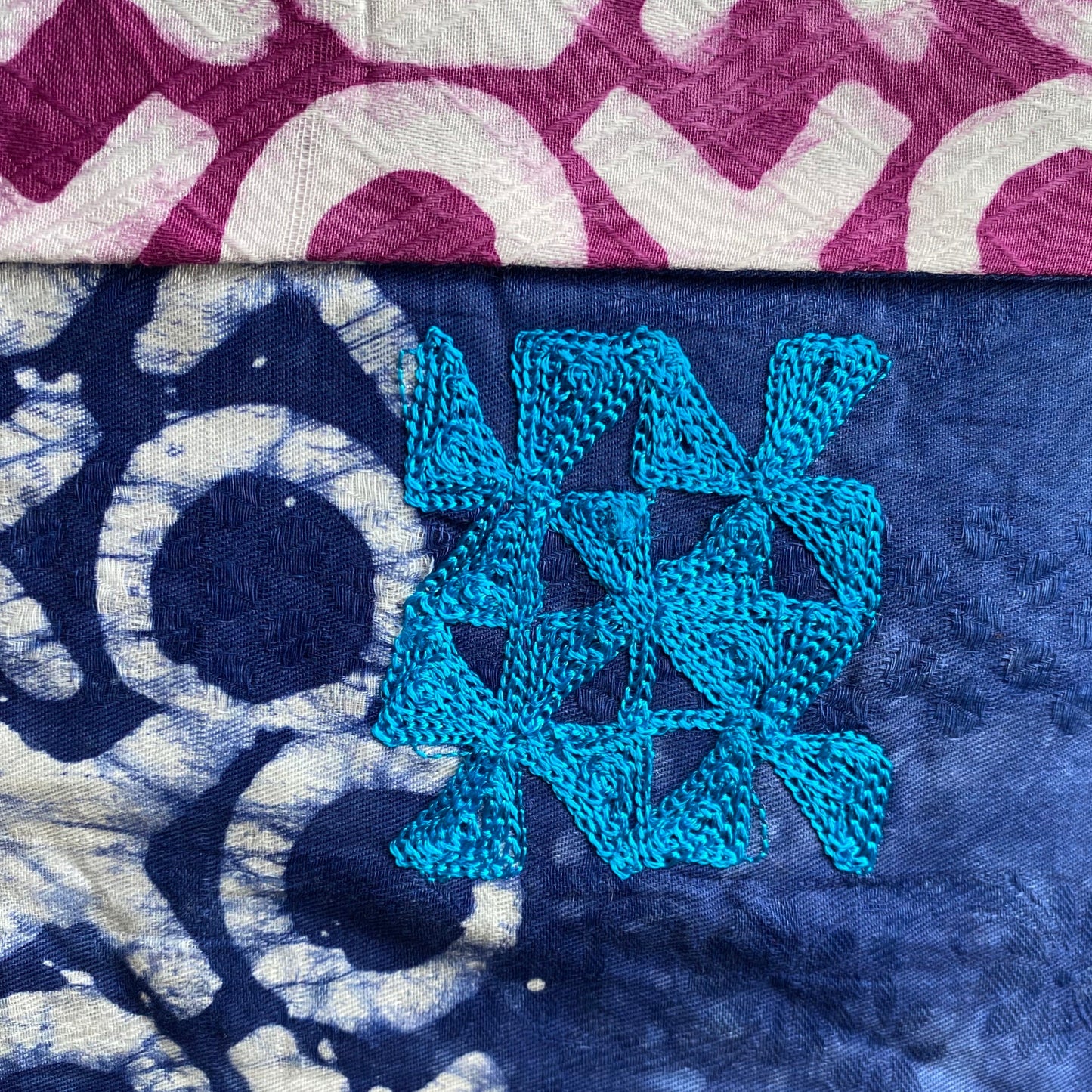 Close up of the reversible 2 different colour hand printed batik geometric patterned scarf with embroidery symbols.