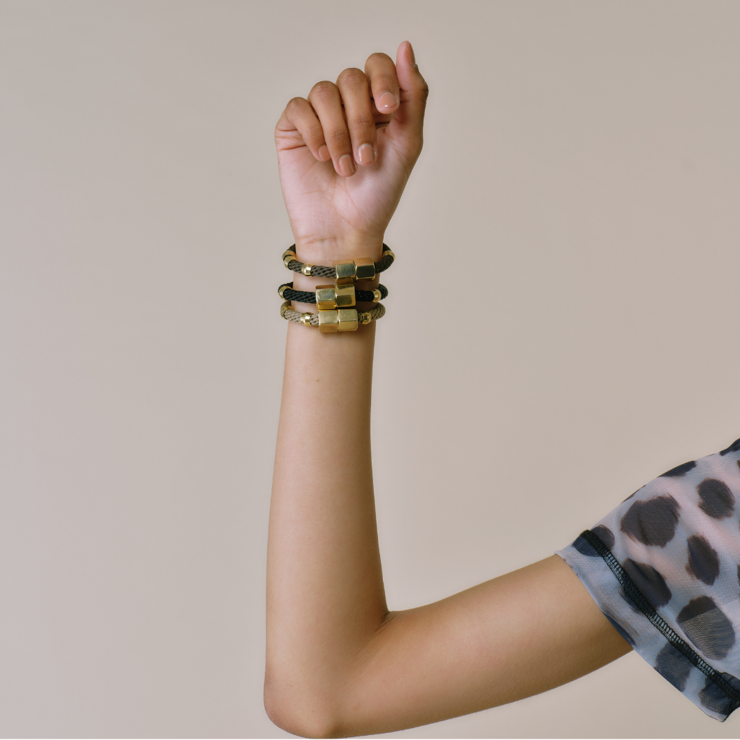 An arm wearing multiple black bracelets with brass details and a magnetic brass clasp.
