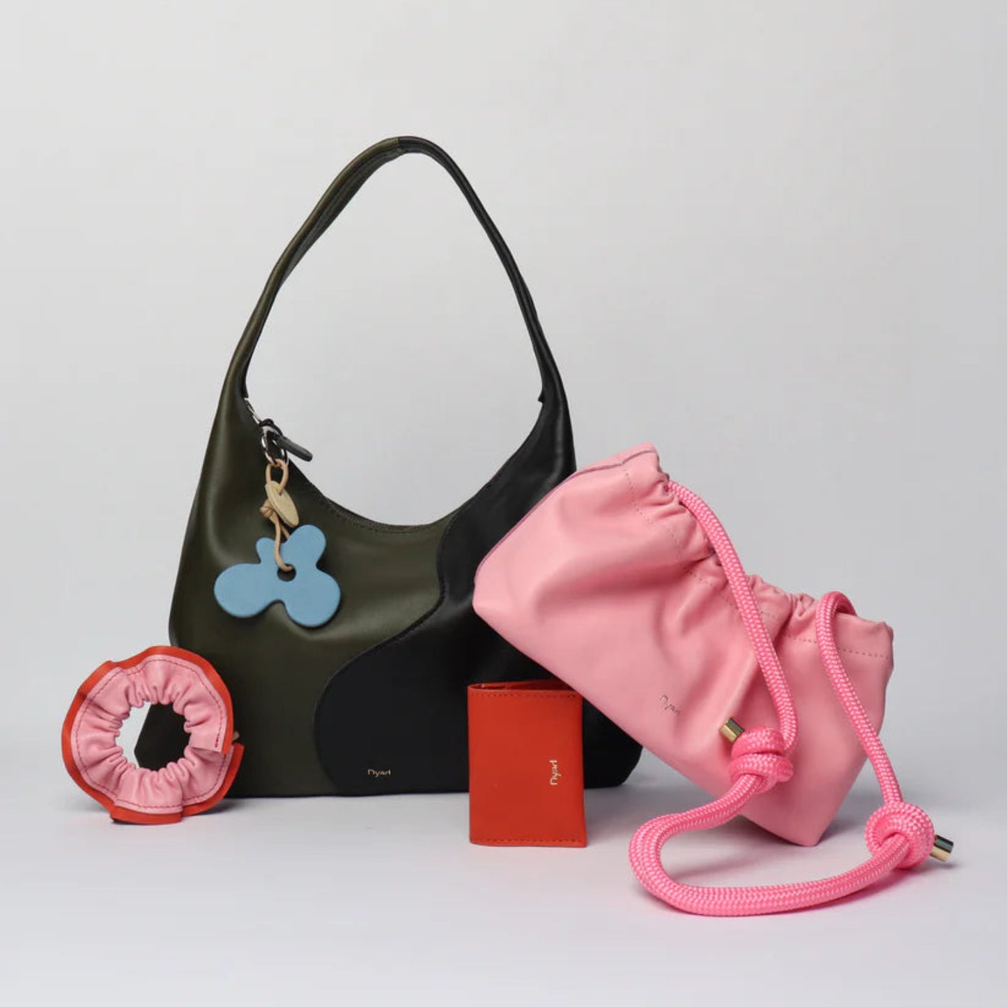 Collection of handbag, Sling handbag with thick braided rope, different keychains, and a cardholder on a light gray background.