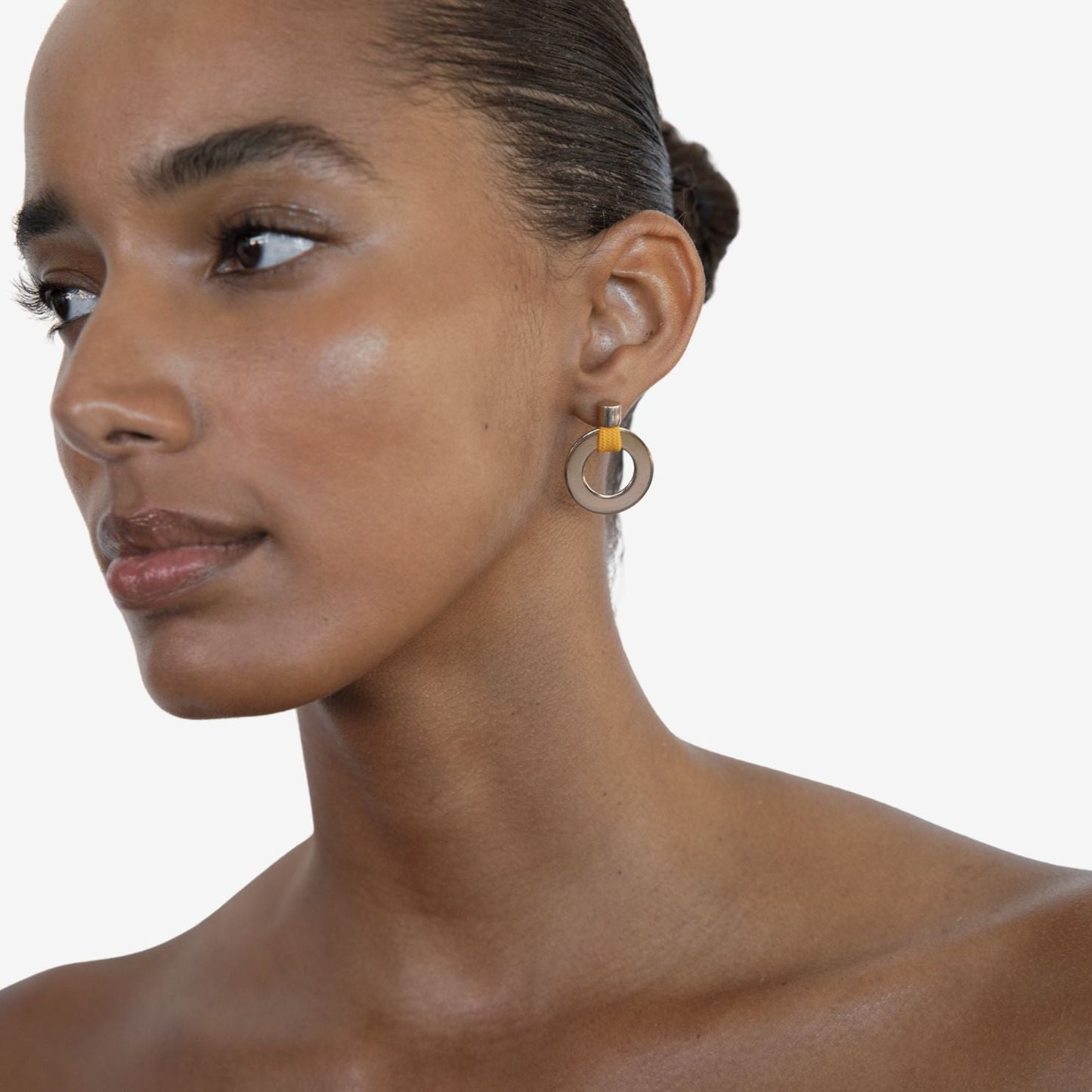 Close-up of a woman wearing a gold earring with a yellow accent on a white background