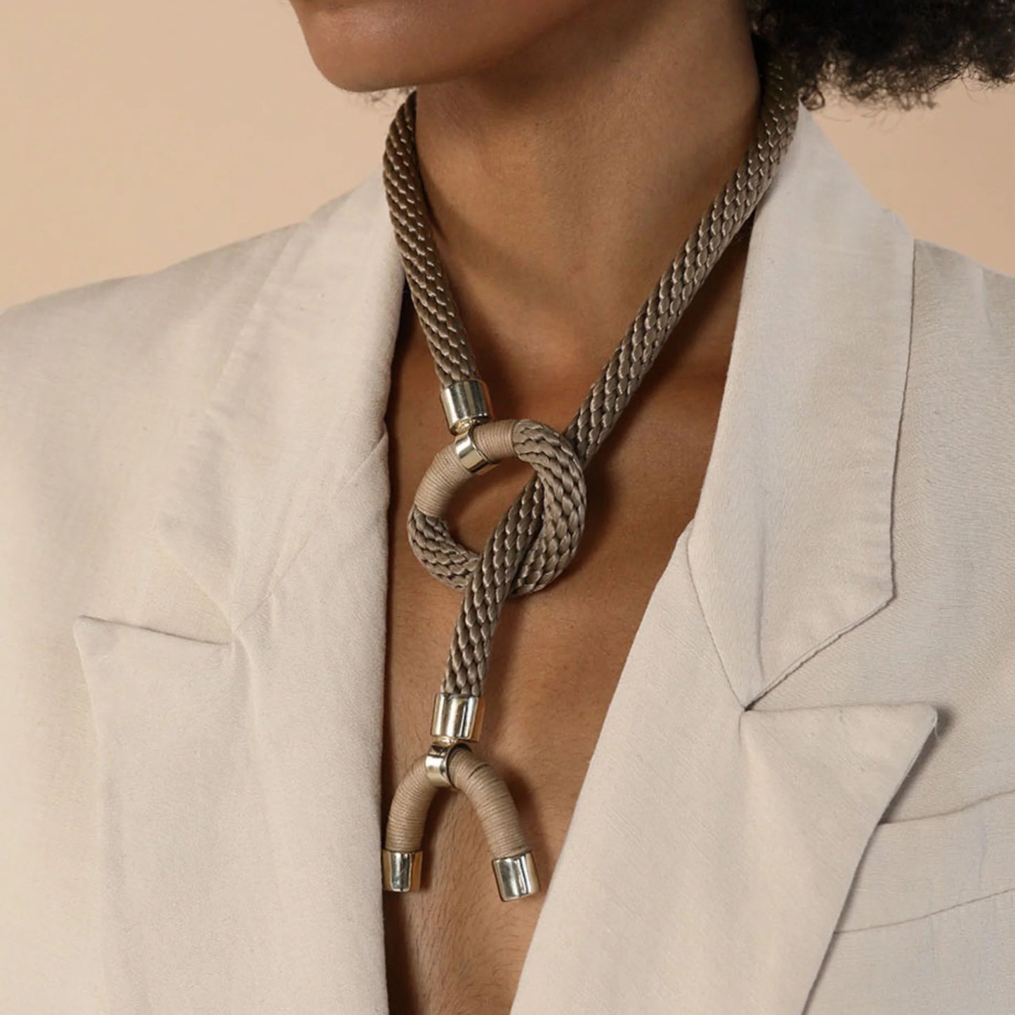 Necklace with a knot design worn by a person in a beige suit against a beige background
