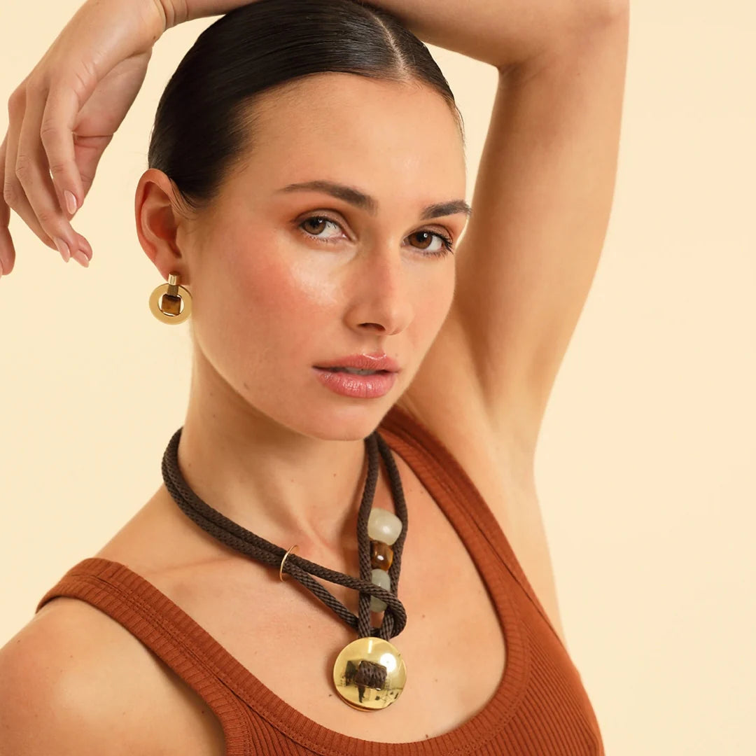 Woman wearing a necklace with gold pendants on a beige background