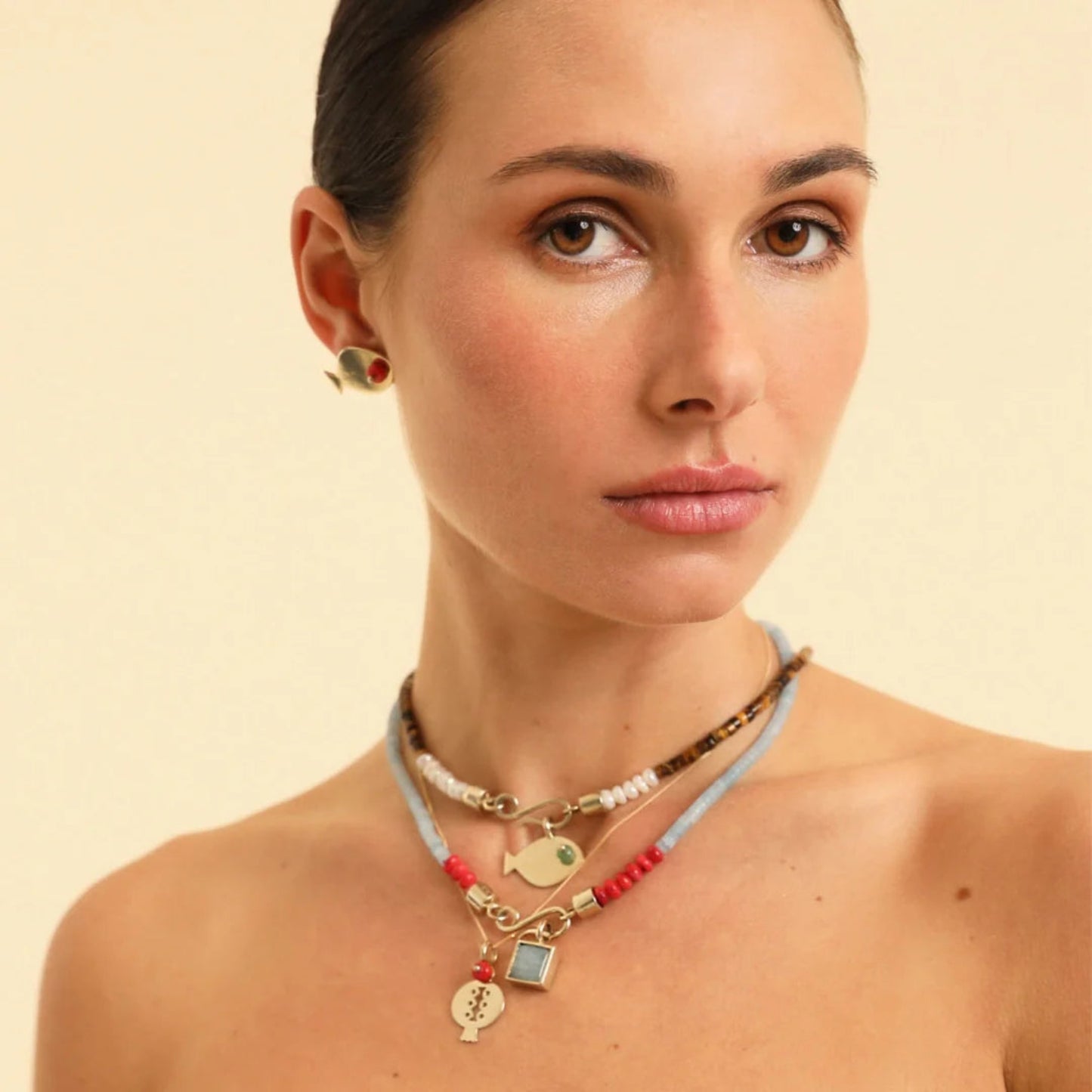 Woman wearing multiple necklaces and earrings on a beige background
