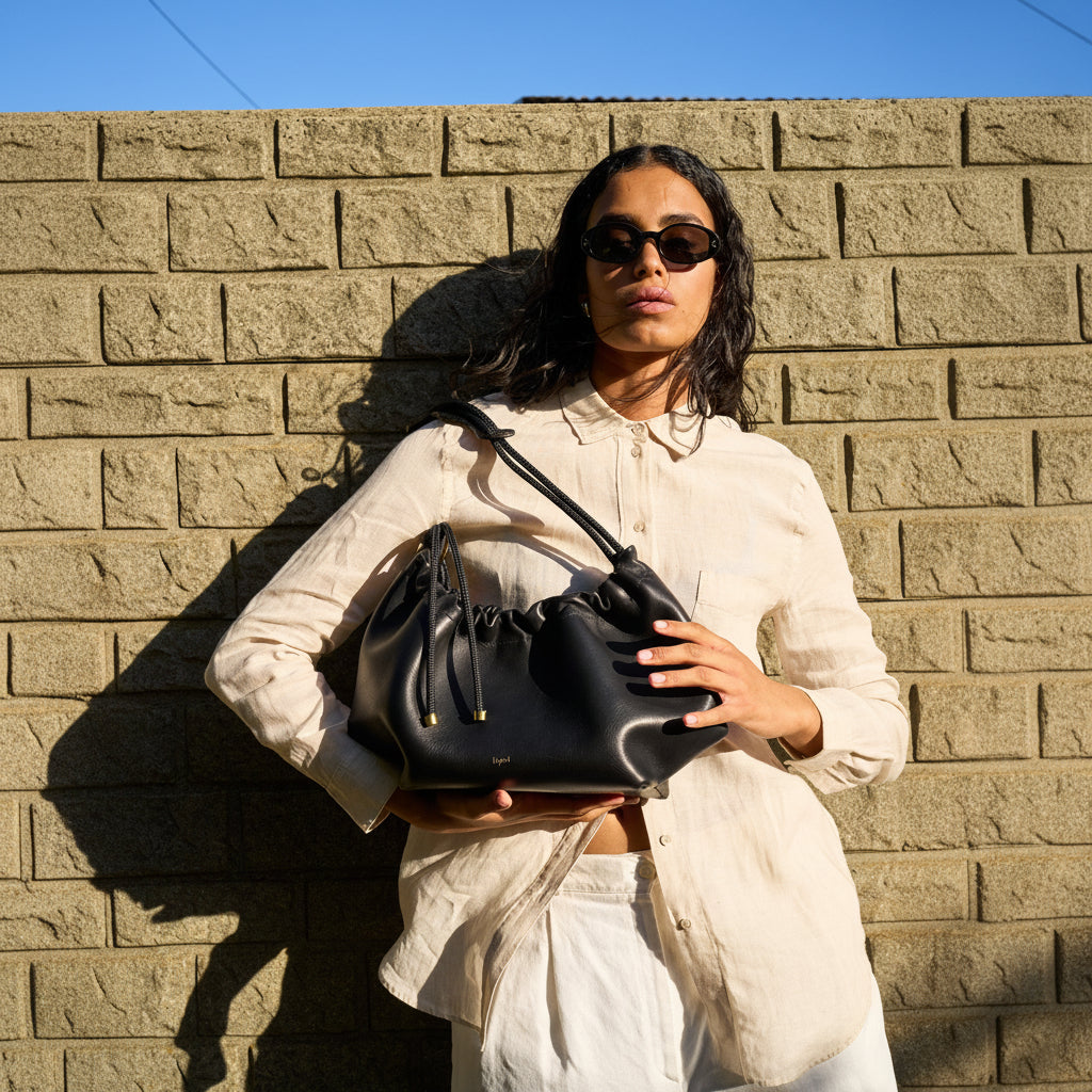 Woman holding a black handbag against a brick wall
