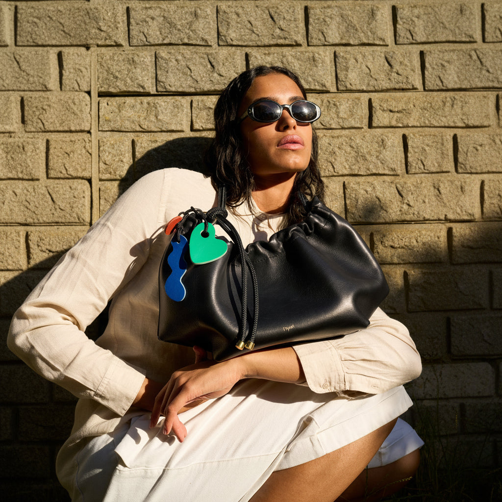 Woman holding a black handbag with colorful keyrings against a brick wall.