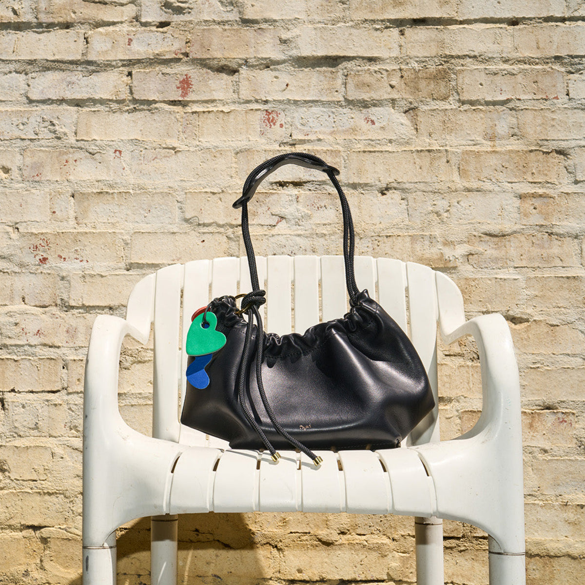 Black handbag with colorful design on a white chair against a stone wall.