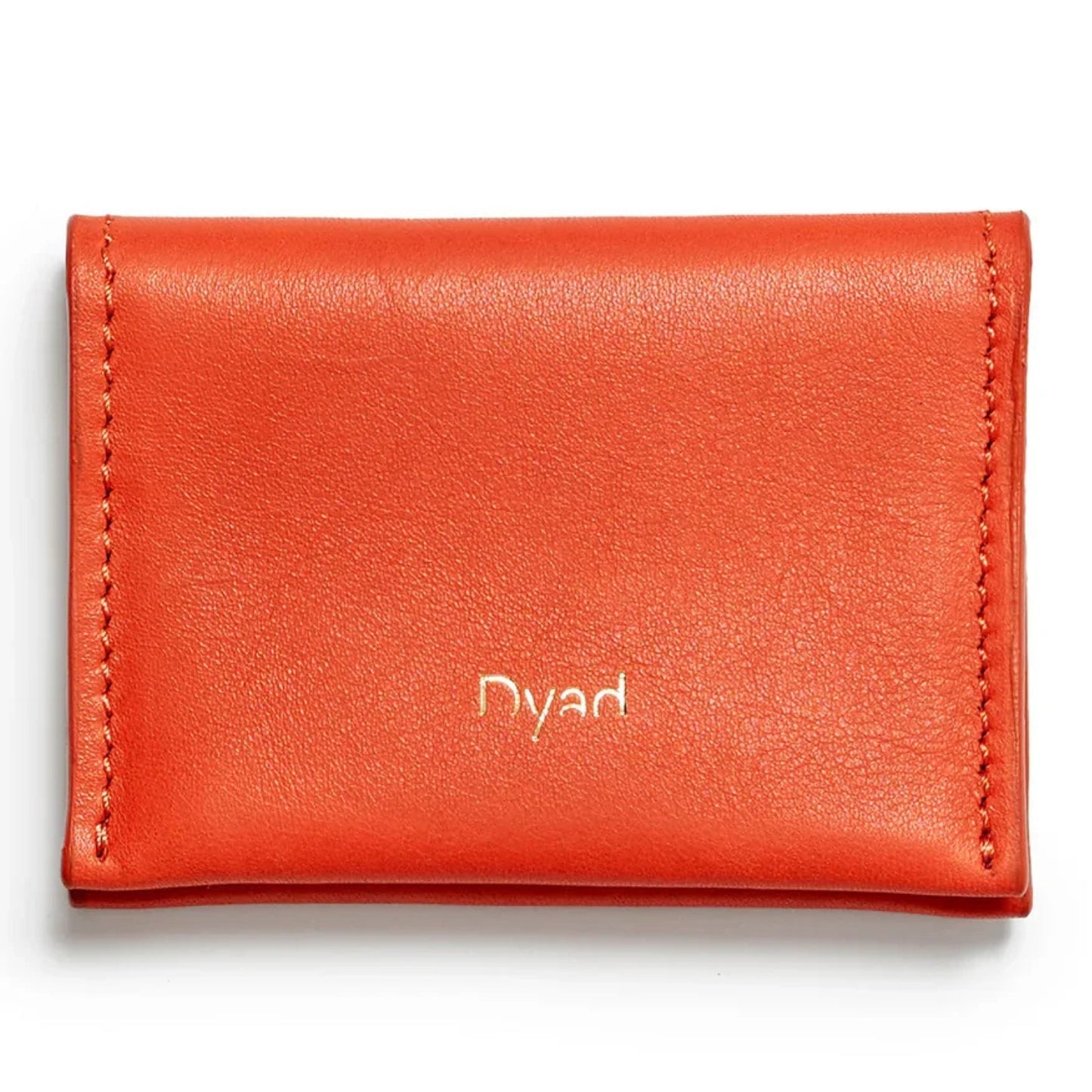 A bright orange-red leather card holder wallet with 'Dyad' embossed in gold on the front.