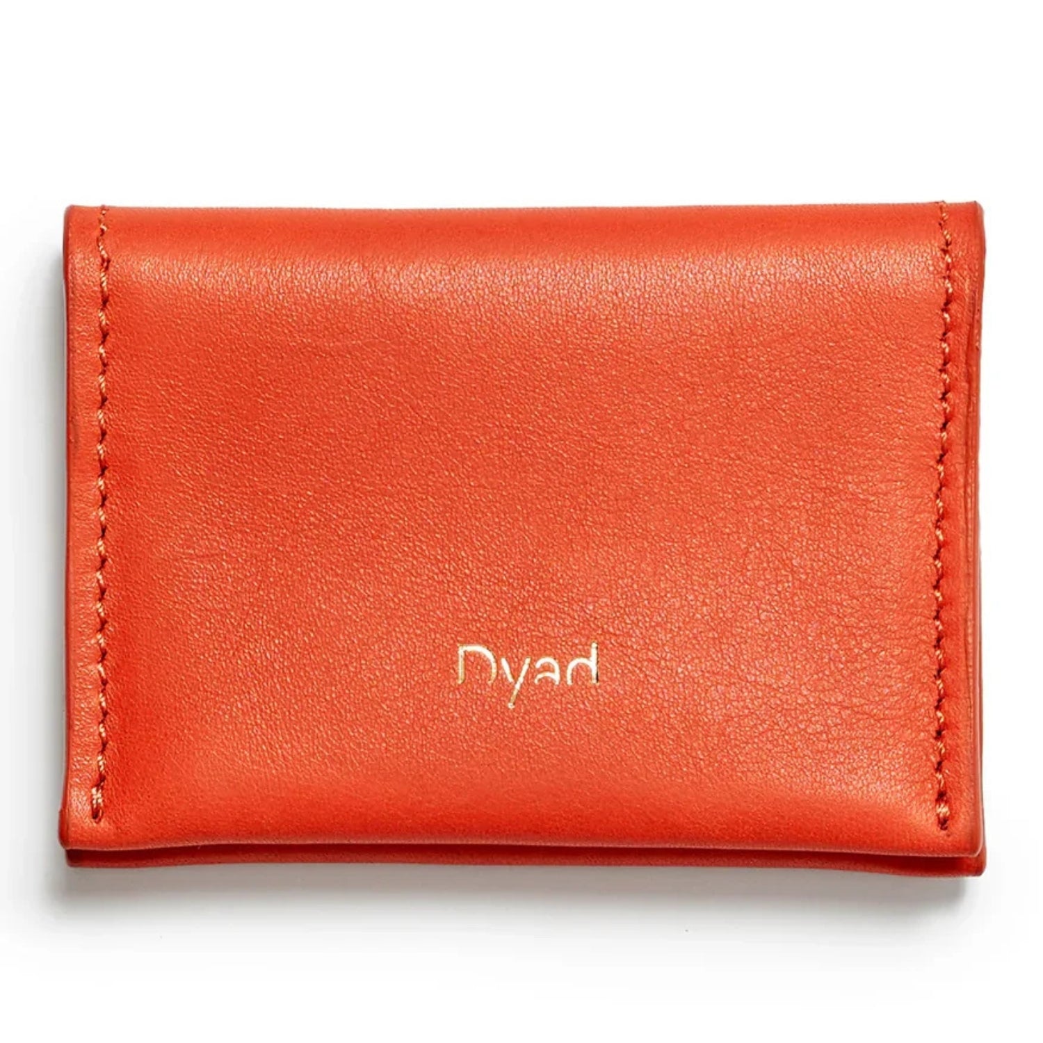 A bright orange-red leather card holder wallet with 'Dyad' embossed in gold on the front.