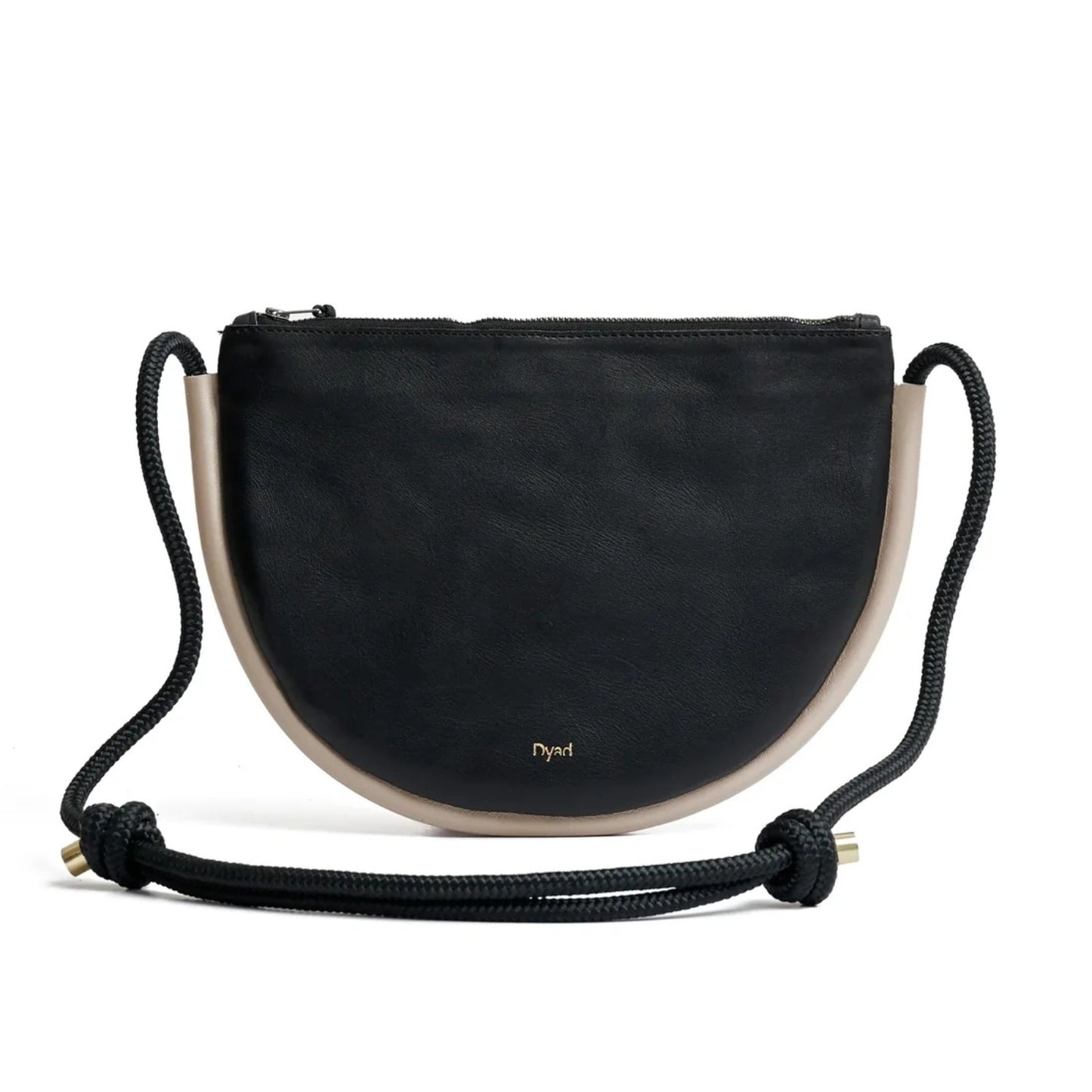 A black and stone trim leather crescent-shaped shoulder bag with a beige leather trim and a black braided rope strap with knotted ends, featuring a small gold 'Dyad' logo on the front.