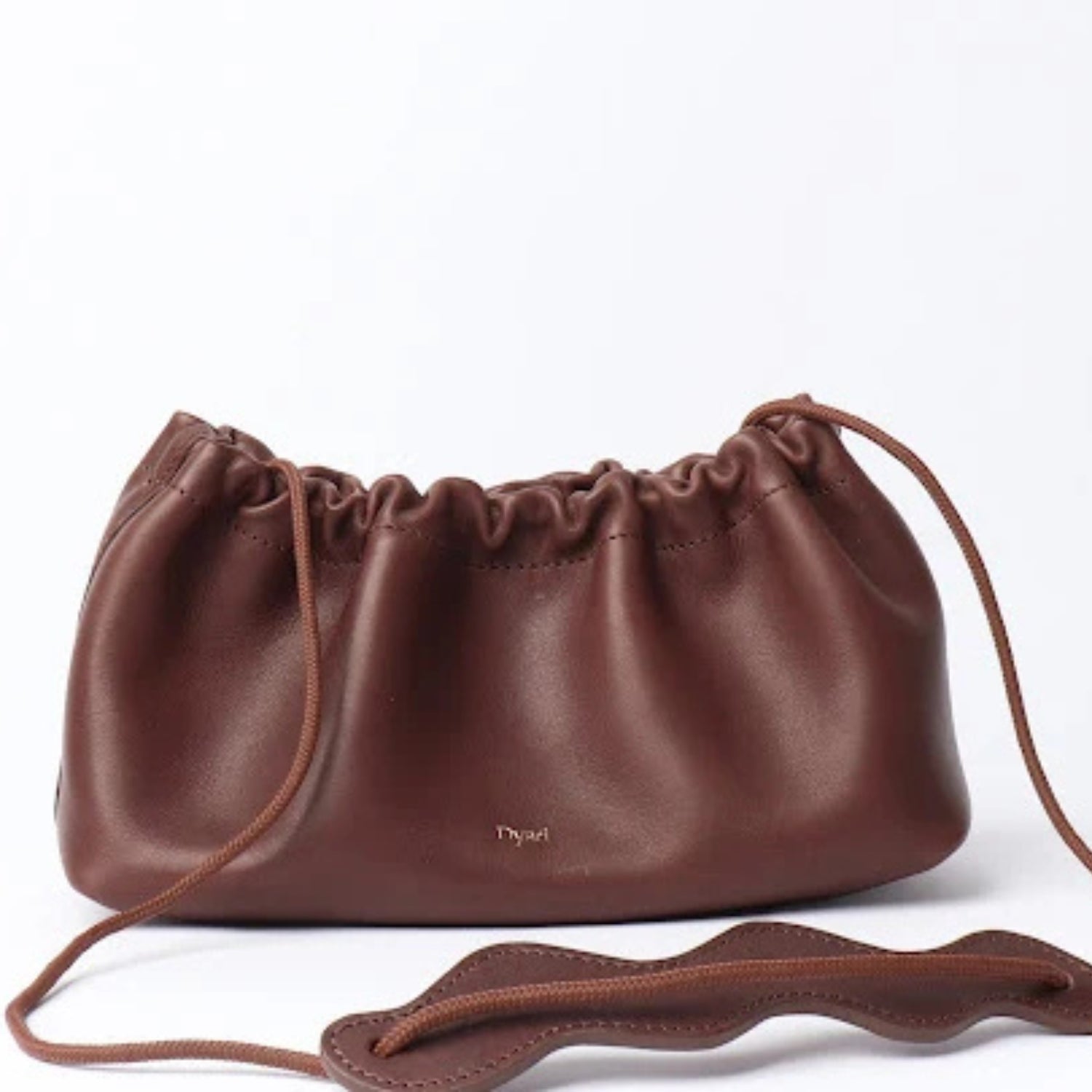 A dark brown leather drawstring bag with a small gold 'Dyad' logo on the front, displayed on a clean white background with its strap draped in the foreground.