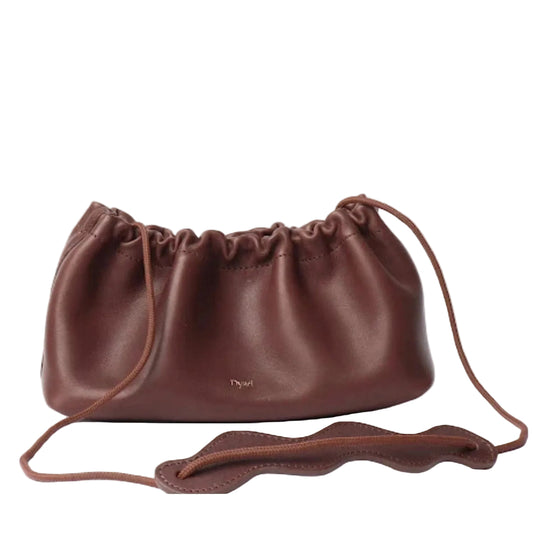 A dark brown leather drawstring bag with a small gold 'Dyad' logo on the front, displayed on a clean white background with its strap draped in the foreground.