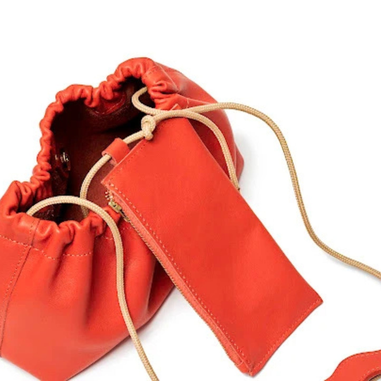 A bright red leather drawstring pouch bag with a matching zippered slip pocket and beige rope drawstrings, shown on a white background.