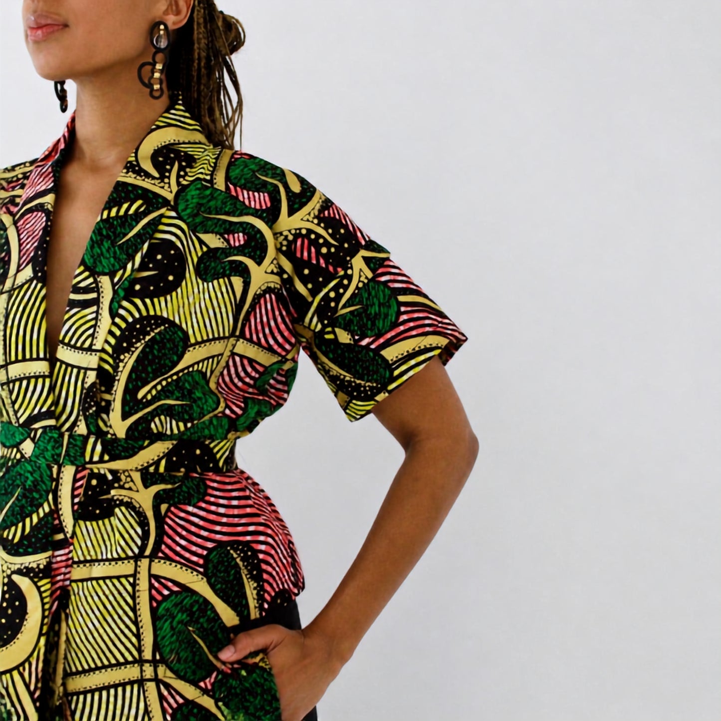 A close-up of a model wearing a short-sleeve wrap-style top with a bold, multicolor African wax print pattern featuring green, yellow, pink, and black.