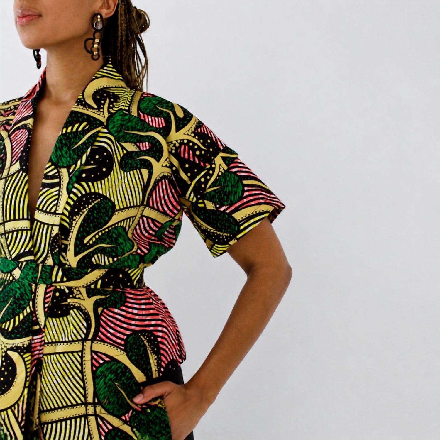 A close-up of a model wearing a short-sleeve wrap-style top with a bold, multicolor African wax print pattern featuring green, yellow, pink, and black.