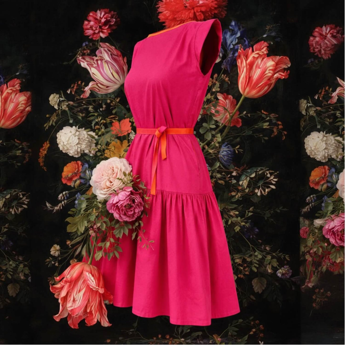 A sleeveless bright pink dress with a matching waist tie, displayed against a dark background surrounded by large colorful flowers.