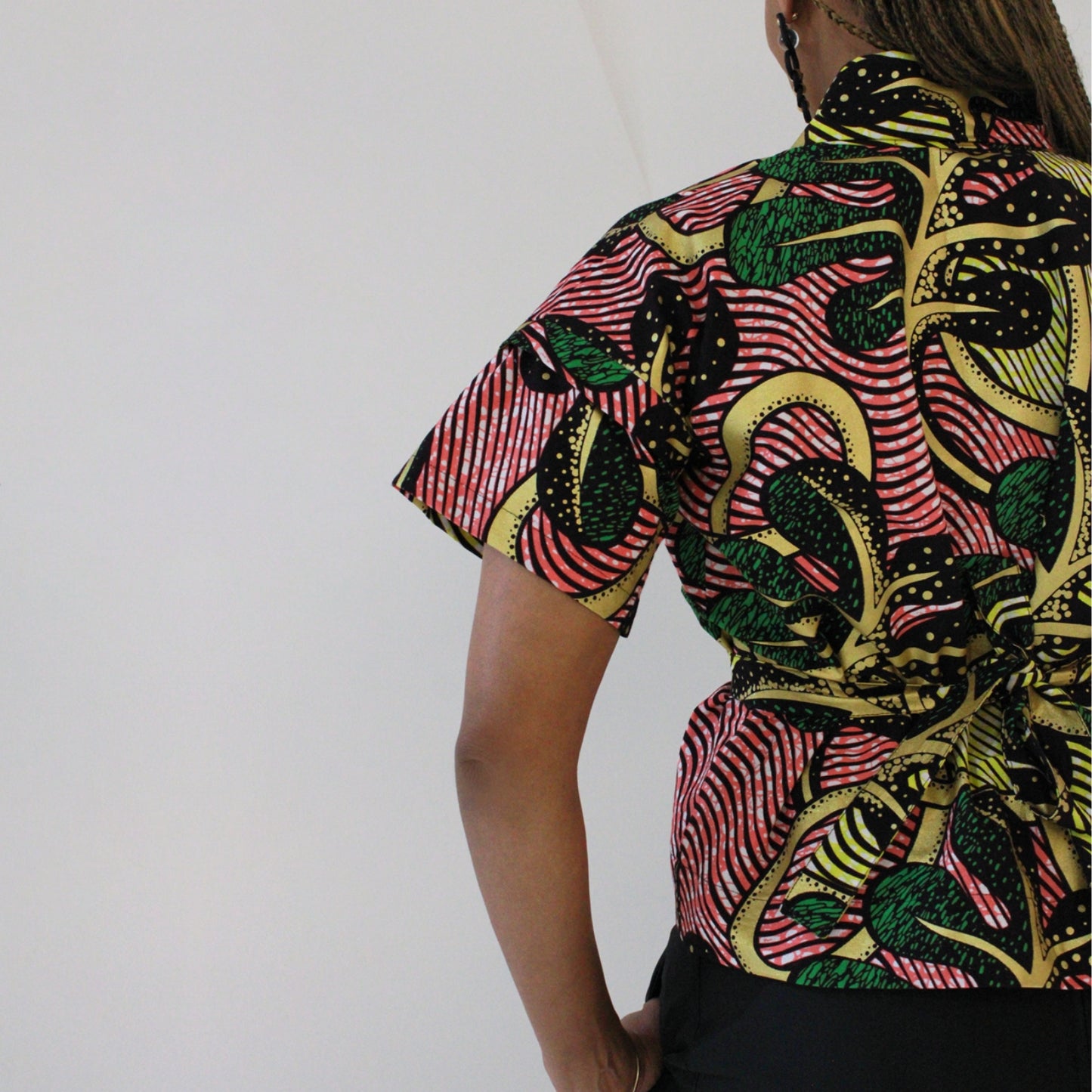 A close-up of a person wearing a short-sleeve African wax print top with a colorful pattern of red, green, black, and yellow.