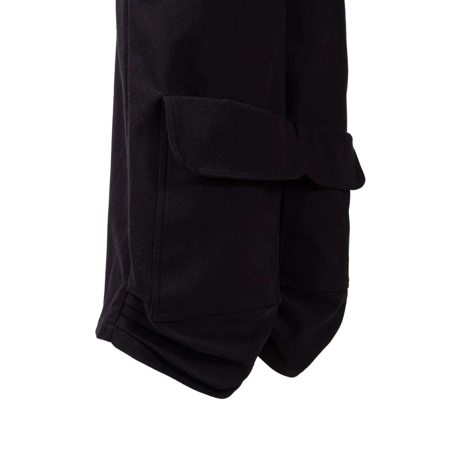 Close-up of black cargo pants showing a side flap pocket and the rolled cuff of the leg against a plain white background.