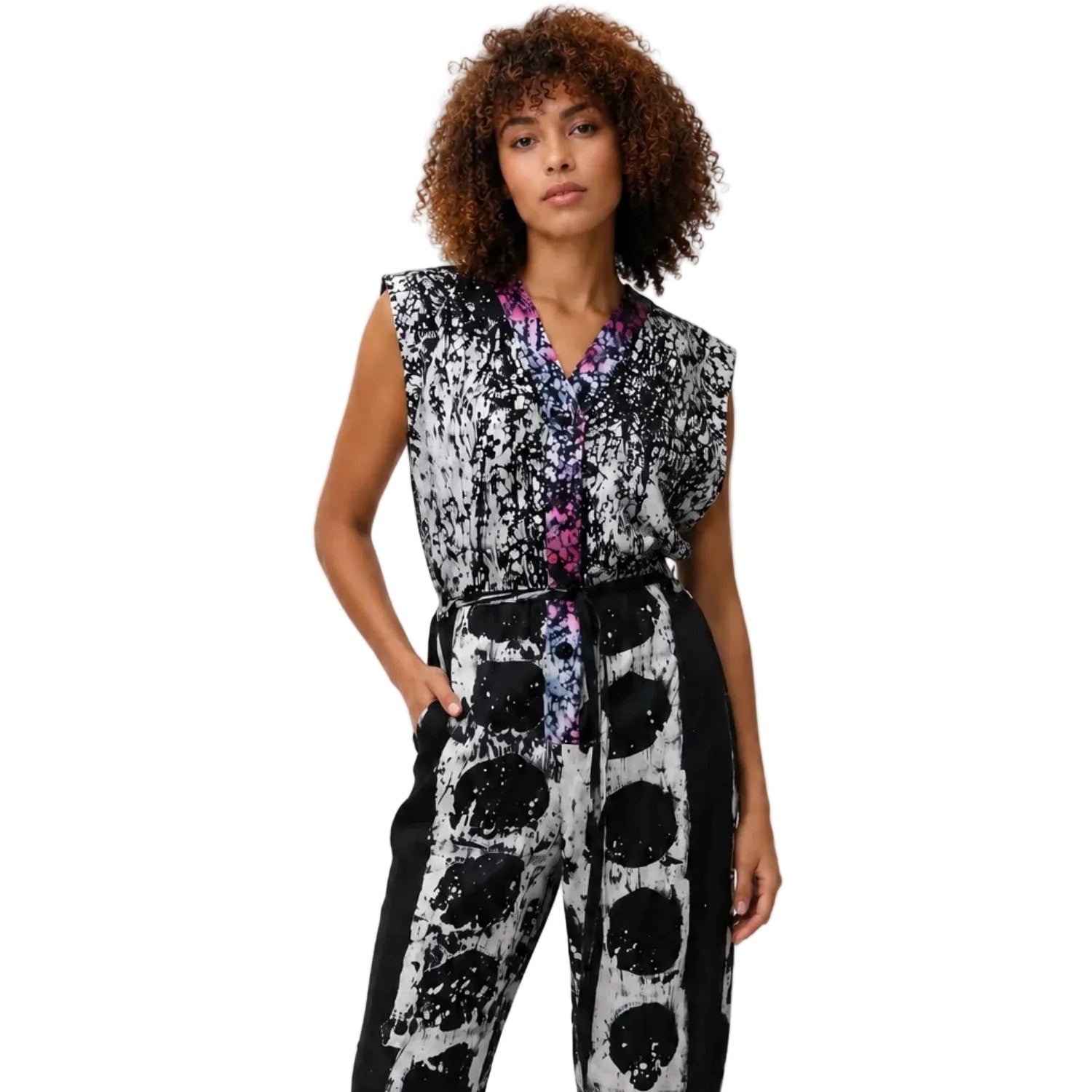 A woman modeling a sleeveless wrap-style jumpsuit with a black, white, and gray abstract print and a purple floral button placket.