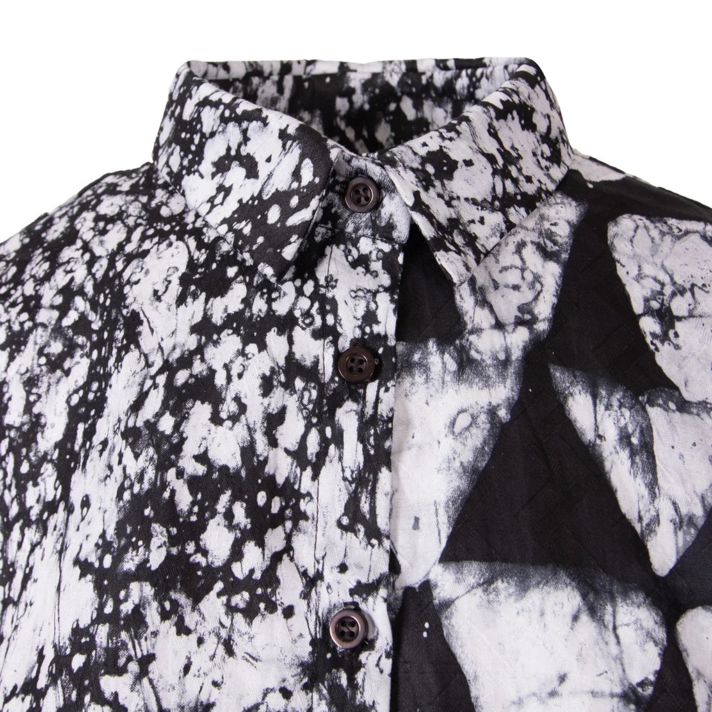 A close-up of a black and white patterned button-down shirt, showing a split design with a black-and-white splatter print on one side and a black-and-white geometric triangle pattern on the other.