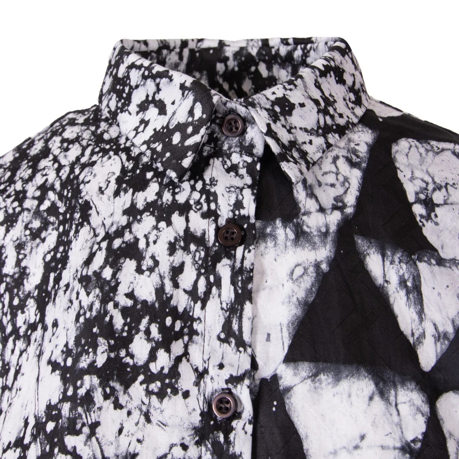 A close-up of a black and white patterned button-down shirt, showing a split design with a black-and-white splatter print on one side and a black-and-white geometric triangle pattern on the other.