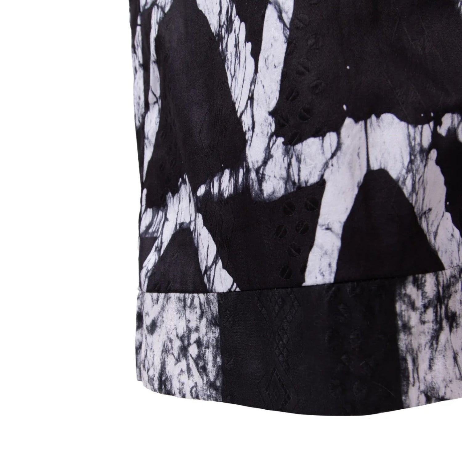 Close-up of a black and white abstract patterned garment, showing textured fabric panels and eyelet embroidery on a white background.