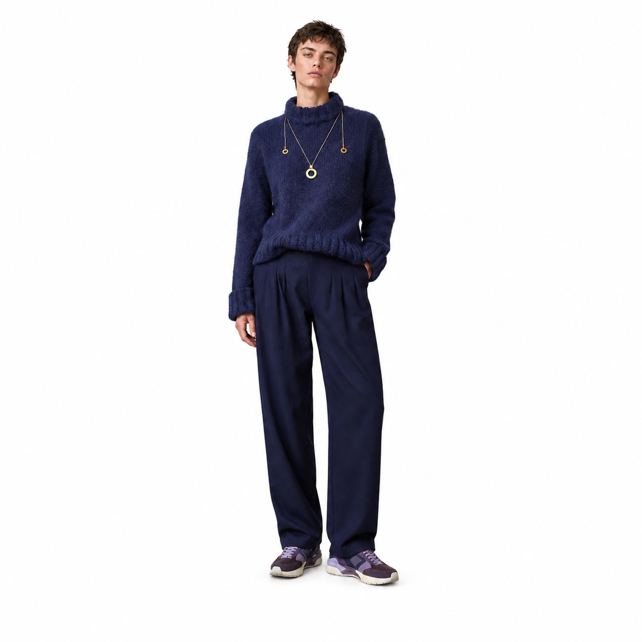 A model stands against a solid white background wearing a navy blue knit mock-neck sweater and matching navy blue sweatpants, accessorized with gold necklaces and purple sneakers.