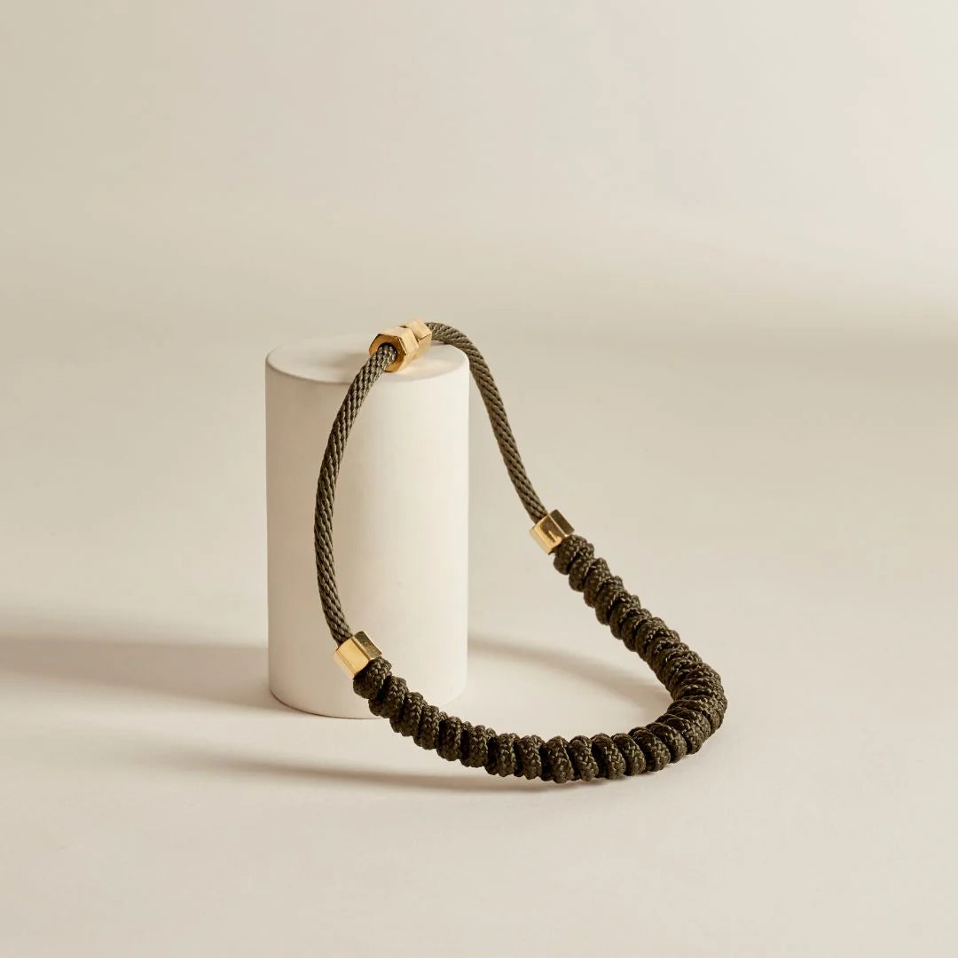 Brown braided necklace with gold accents on a white cylindrical stand against a beige background