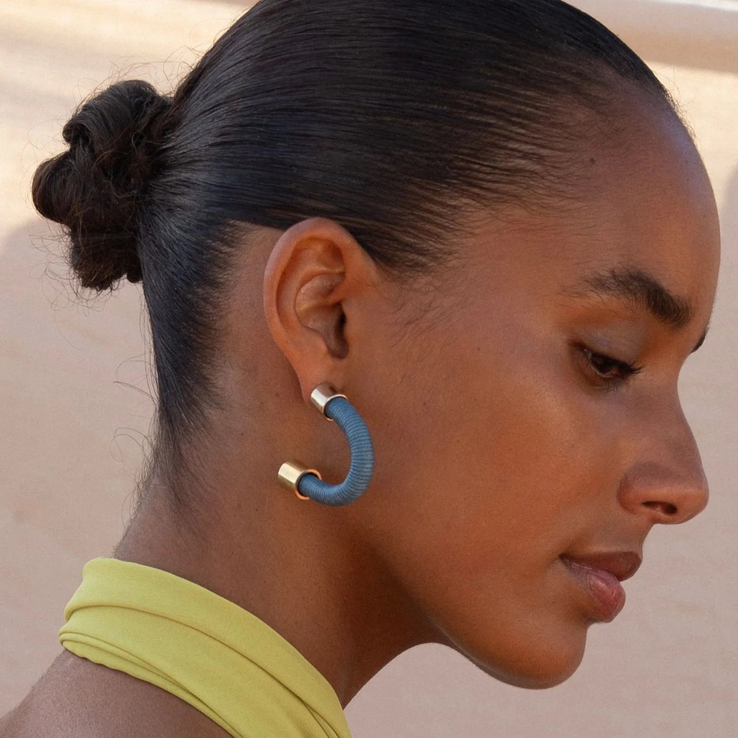 Close-up of a woman wearing a blue hoop earring with a neutral background