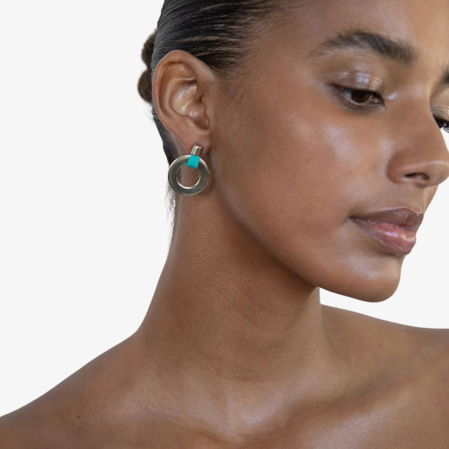 A close-up of a woman wearing a silver-toned ring earring with a small turquoise accent on the post, shown against a plain light background.