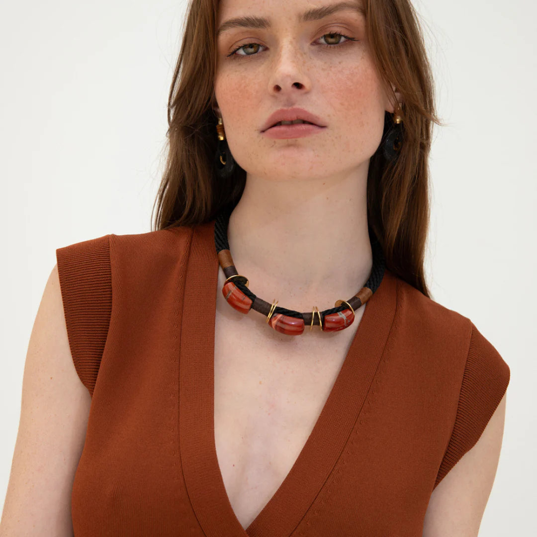 A woman wearing a brown dress and a black and red jasper choker with brass discs and a wax cord.