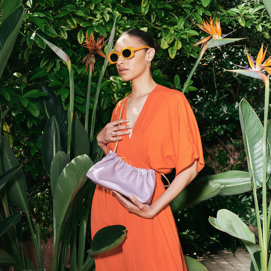 Woman in an orange dress holding a purple clutch amidst tropical plants