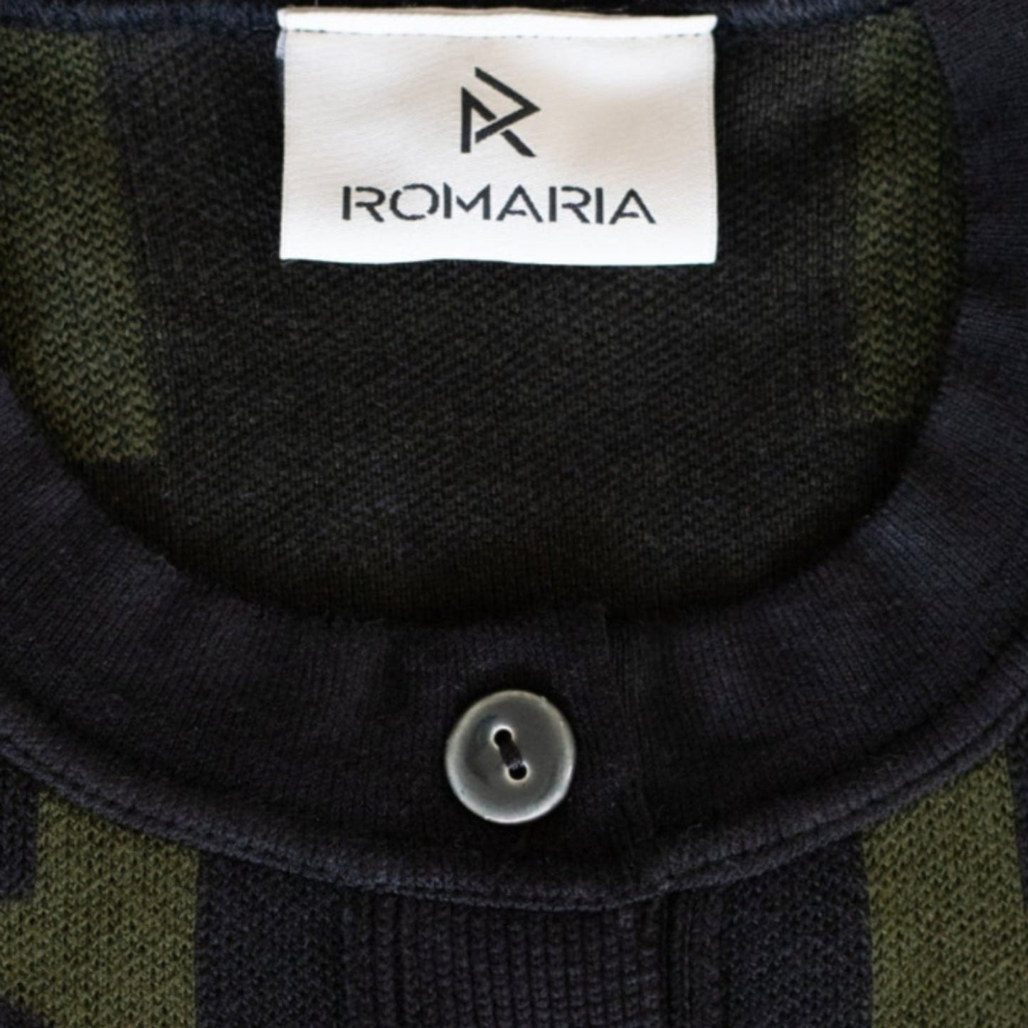 Close-up of a Romaria knit cardigan featuring a dark and olive green geometric pattern, a ribbed mock neck, and a white brand label.