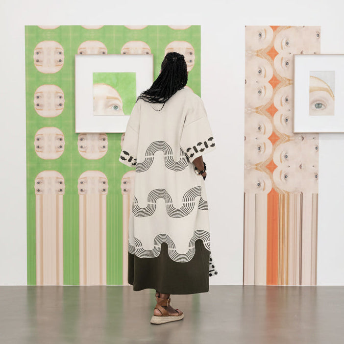 A white long-sleeve t-shirt with a black and white graphic print of a woman in a black hat and coat, displayed against a background of green and white vertical stripes.