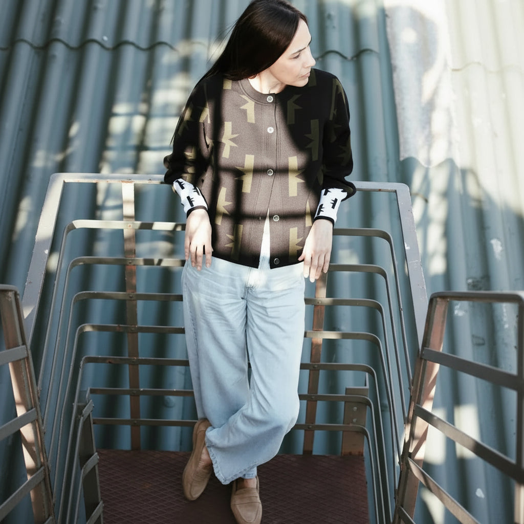 A woman wearing a black and olive patterned cardigan, light blue jeans, and brown suede boots, standing on an outdoor metal staircase.