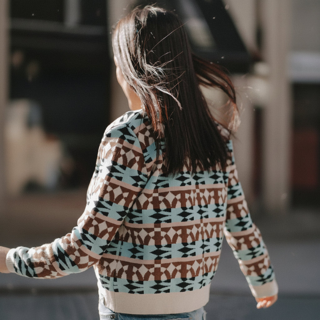 A person viewed from behind wearing a long-sleeve knit sweater with a brown, beige, and light blue geometric pattern.