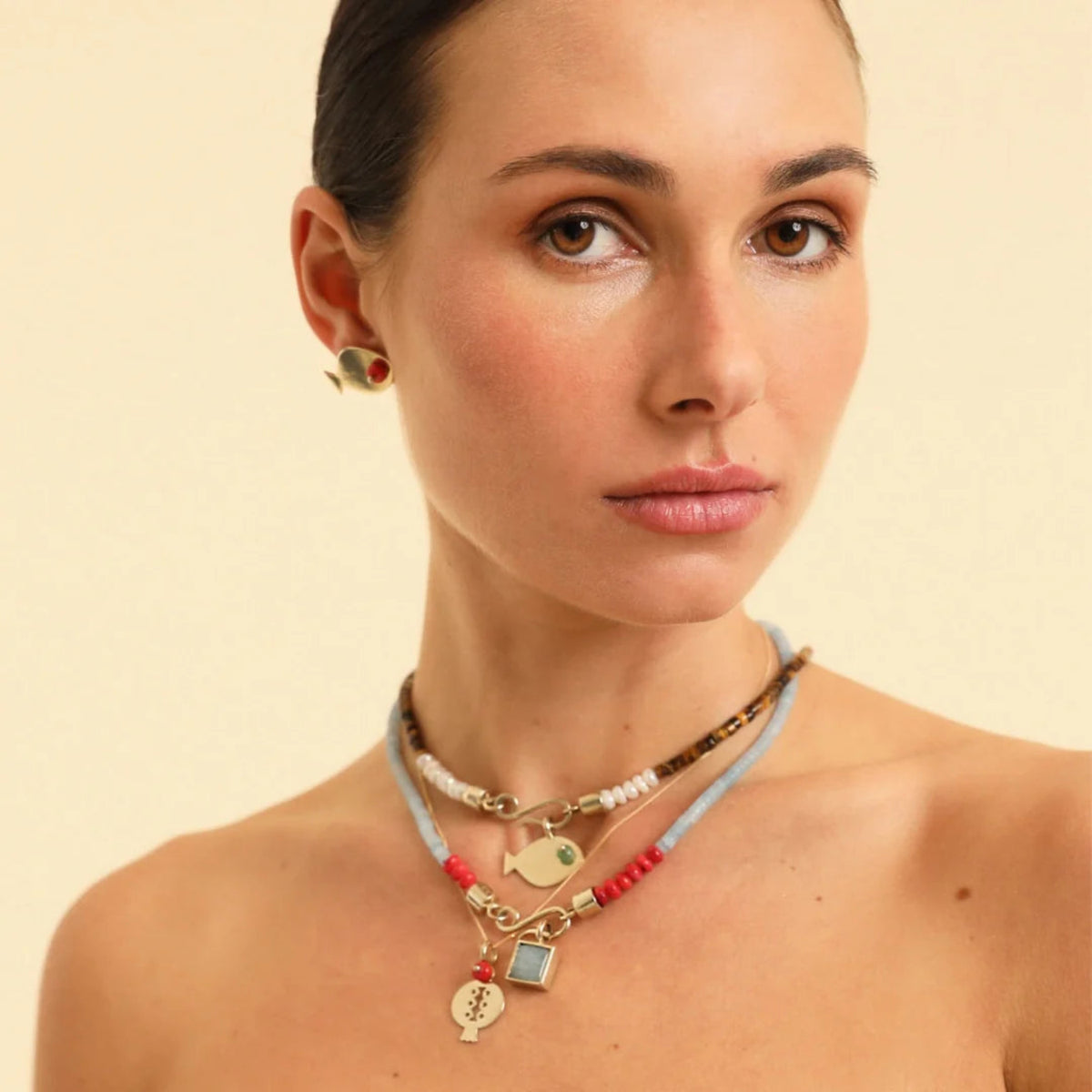 Woman wearing multiple necklaces and earrings on a beige background