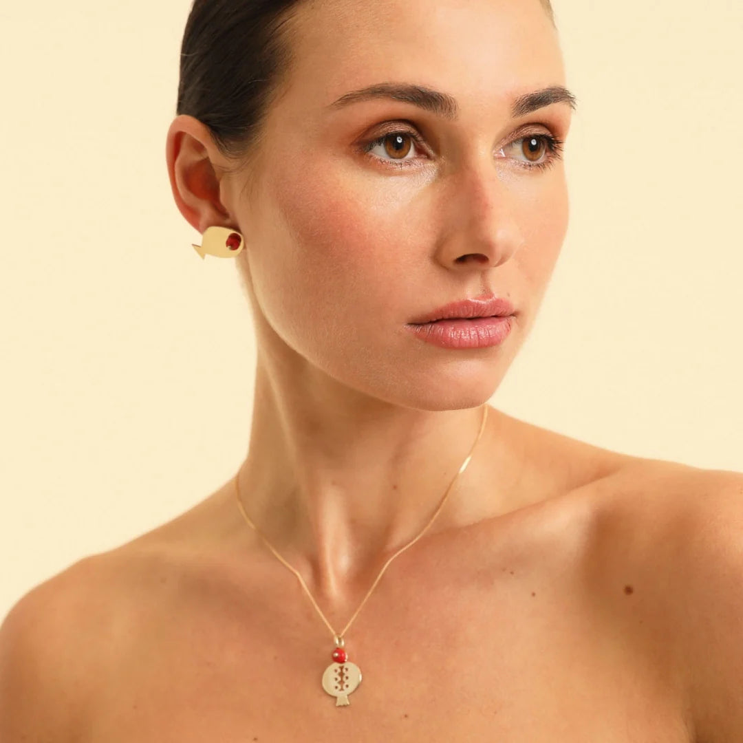 Woman wearing a gold necklace with a pendant against a beige background