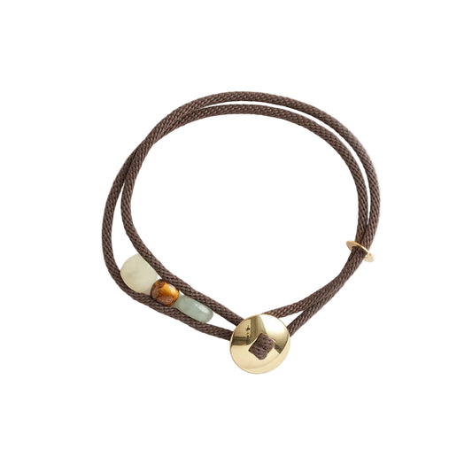 Brown cord bracelet with gold and gemstones on a white background