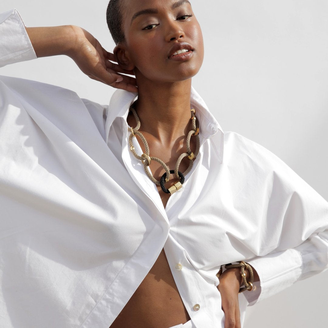 A woman wearing a white shirt and beige necklace with black accents.