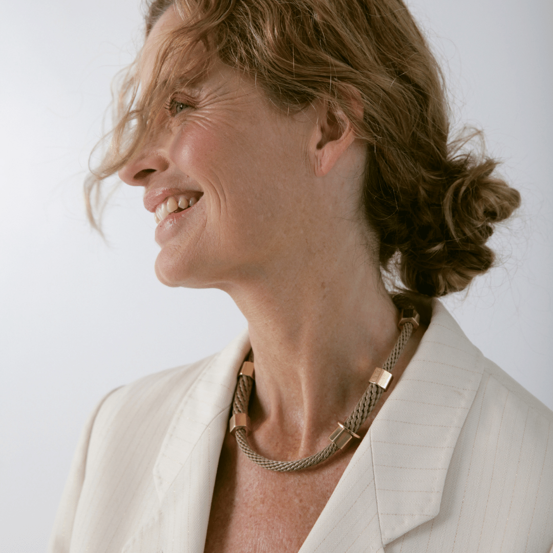 A person wearing a beige choker necklace with brass caps and a textured rope design.
